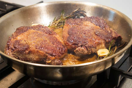 Ribeye beef steak in a stainless steel pan with butter.