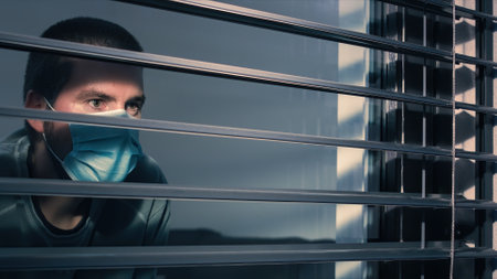 Coronavirus lockdown. Man with face mask looking through window.の写真素材