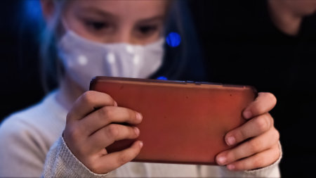 Girl child playing with smartphone wearing face mask at coronavirus lockdown.の写真素材