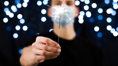 Man with face mask holding sparkler for christmas and new year party.の写真素材