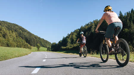 Woman and girl child riding mountain bikes on a country road in nature on a bright sunny summer day.の写真素材