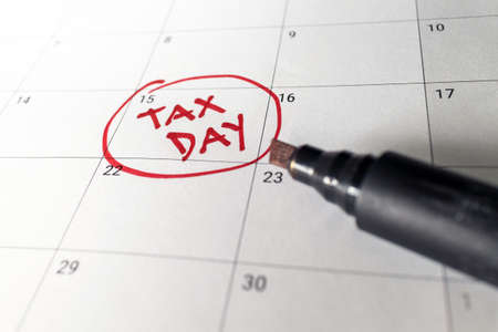 Writing tax day on April 15 calendar with red marker. Deadline for 1040 form return.