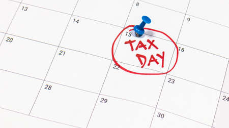 Pinning tax day on April 15 calendar and marked in red. Deadline for 1040 form return.の写真素材