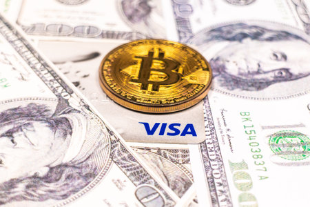SLOVENIA, LJUBLJANA - March 2, 2021: Bitcoin coin and Visa credit card on dollar bills.のeditorial素材