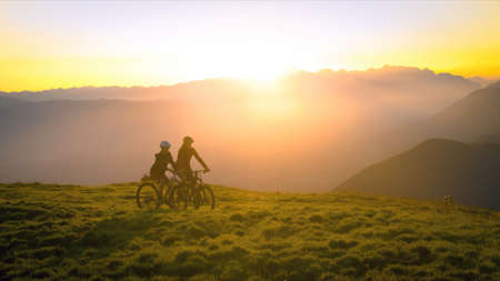Mother and daughter cycling uphill with mountain bikes at a sunset.の写真素材