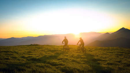 Mother and daughter cycling uphill with mountain bikes at a sunset.