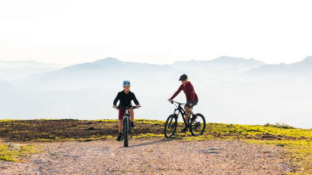 Mother and daughter cycling uphill with mountain bikes at a sunset.の写真素材