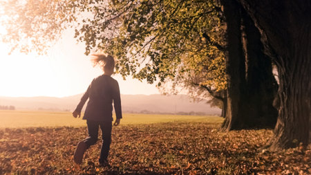 Preschool girl running on the dry leaves at the edge of the forest, on a beautiful autumn dayの写真素材