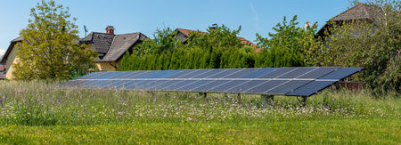 Solar panels on green meadow next to houses.の写真素材