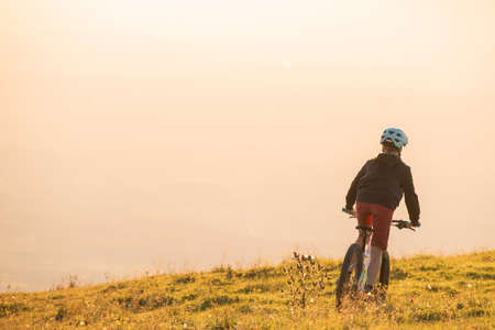 Girl child riding mountain bike into the sunset. Beautiful golden summer light.の写真素材