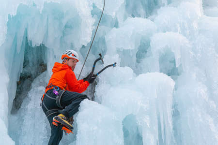 Athlete climb frozen waterfall, swinging the axe pick into the ice and using it as a grip to pull himself upの写真素材