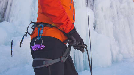 Ice climber, with gloved hands, tying a rope to his harness