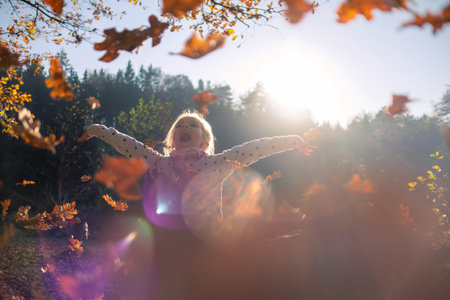 Smiling girl child throwing dry leaves in the air at beautiful autumn sunset.の写真素材