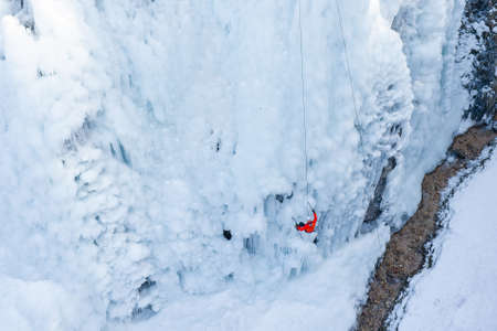 Birds eye view shot of a Caucasian male athlete climbing down the side of an icy slope, using rope attached to his harnessの写真素材