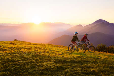 Mother and daughter cycling on mountain bikes at a sunset in mountains.の写真素材