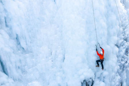 Aerial view of a frozen waterfall and rocks with climber ascending its ice-covered surface, using ice axes and cramponsの写真素材