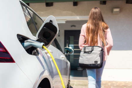 Electric car charger plugged in, with a female silhouette in the background