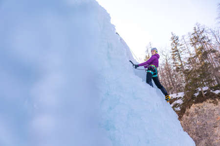 Female ice climber silhouette swinging axes into the ice with force, the shattered ice fallingの写真素材