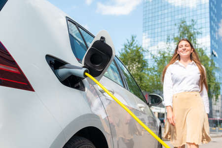 Smiling woman unplugging the electric car charger at a downtown charging pointの写真素材