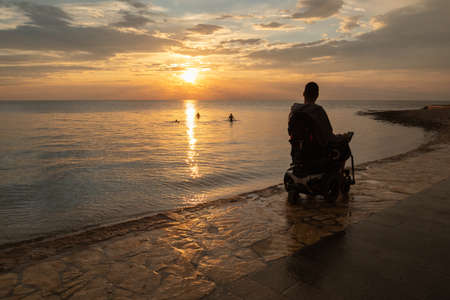 Disabled person in a wheelchair at sunset looking at sea.の写真素材