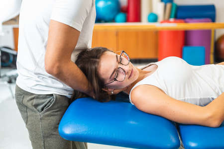 Man hands doing manual joint neck stretching and giving a neck massage to a young Caucasian womanの写真素材