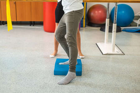 Male patients legs doing balance pad exercises with the assistance of a female therapist.