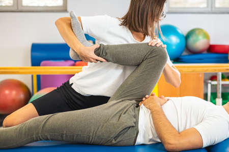 Woman physiotherapist giving a rehabilitation leg and hip treatment to a male patient.