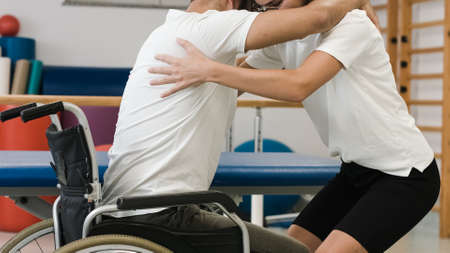 Person with disability and female physiotherapist, exercise standing up and proper lifting technique from a wheelchair.の写真素材