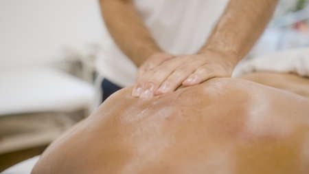 Masseurs hands giving a back massage to female patient using oil.