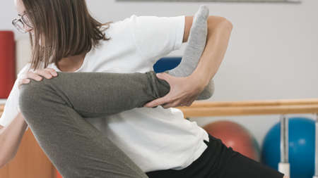Woman physiotherapist giving a rehabilitation leg and hip treatment to a male patient.の写真素材