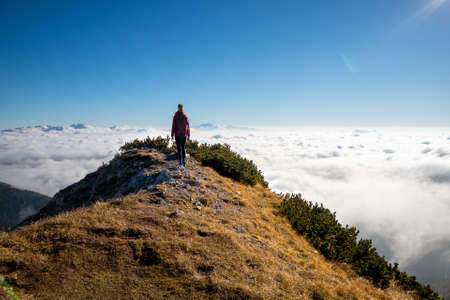 Woman on top of the mountain above the clouds bathing in sunlight.