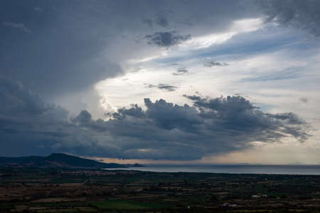 Dark storm clouds above a Mediterranean landscape inland, in the distance visible the sea.の写真素材