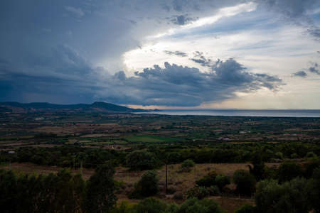 Dark storm clouds above a Mediterranean landscape inland, in the distance visible the sea.の写真素材