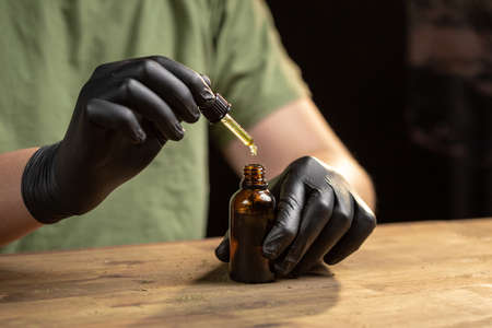 Hands dripping CBD oil drops in glass bottle with a pipette.の写真素材
