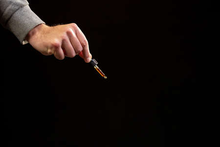 Holding dropper with medical cannabis CBD oil for oral apply. Hemp oil droplets fall from pipette...