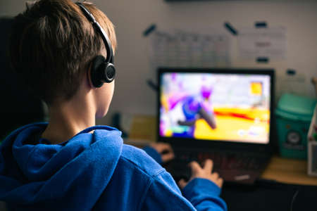 Child gaming on laptop playing addictive online video game at home in his room.