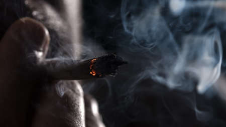 Holding and smoking a marijuana weed joint, inhaling smoke, and blowing it out. Medical Cannabis.の写真素材