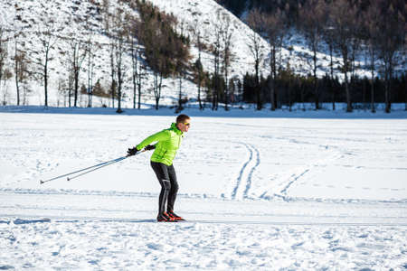 Mature man cross country skiing, on the ski trail surrounded by mountains and forest.の写真素材