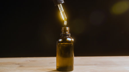 Hand dripping CBD hemp oil with pipette, on the black background.