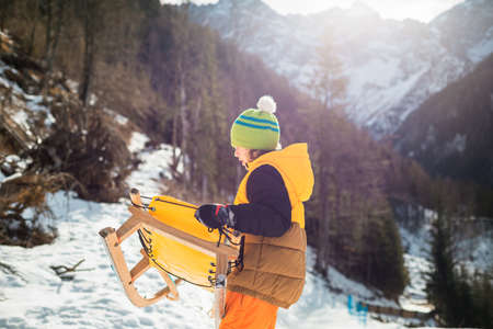 Boy with sleds having fun and playing with snow in the Alpine foothill.の写真素材