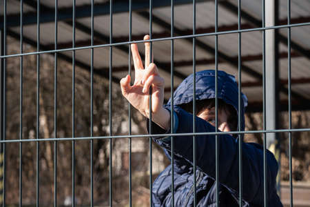 Child refugee hand holding a metal fence. Social problem of war migrants.の写真素材