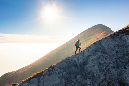 Mountaineering on the mountain, a young woman hiking on the trail with trekking poles on the top of...