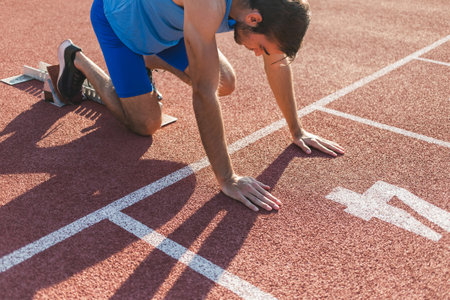 Young professional male athlete in blue sportswear taking a start position for a sprint run during outdoor trainingの写真素材