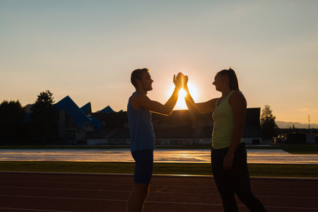 Young sport couple training on athletic stadium giving high five at sunsetの写真素材