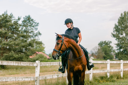 Girl in an equestrian outfit enjoying riding horseback along the trail, smiling and petting her beautiful red horseの写真素材