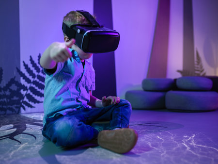 Little boy wearing VR headset sitting on the floor in the museum playroom, engaged exploring virtual...