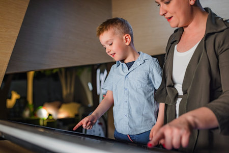 Smiling little boy having fun during a museum visit with his mom, curiously watching interactive...