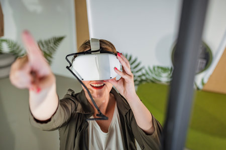 Smiling and delighted young woman enjoying VR experience, using virtual reality glasses in the...