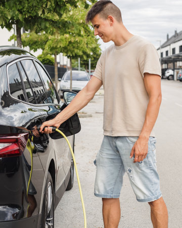 Man opening a socket and putting a charger in a black electric car at an EV charging station placed on city streetの写真素材