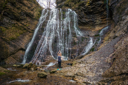 Fit young woman practicing yoga in beautiful waterfall scenery. Concepts of holistic experience, people and nature connection.の写真素材